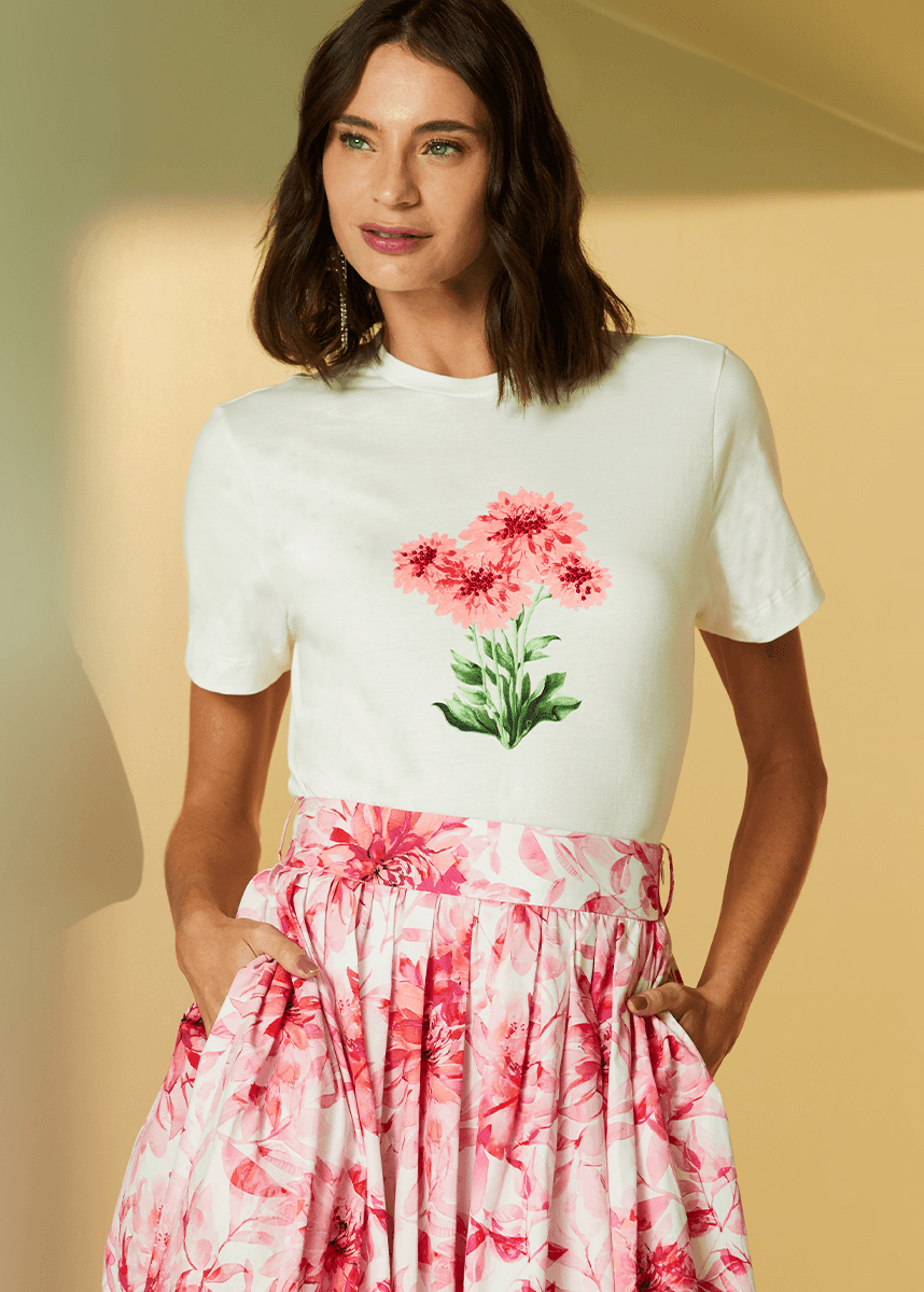 Woman wearing a white t-shirt with pink floral design and a pink floral skirt against a beige background