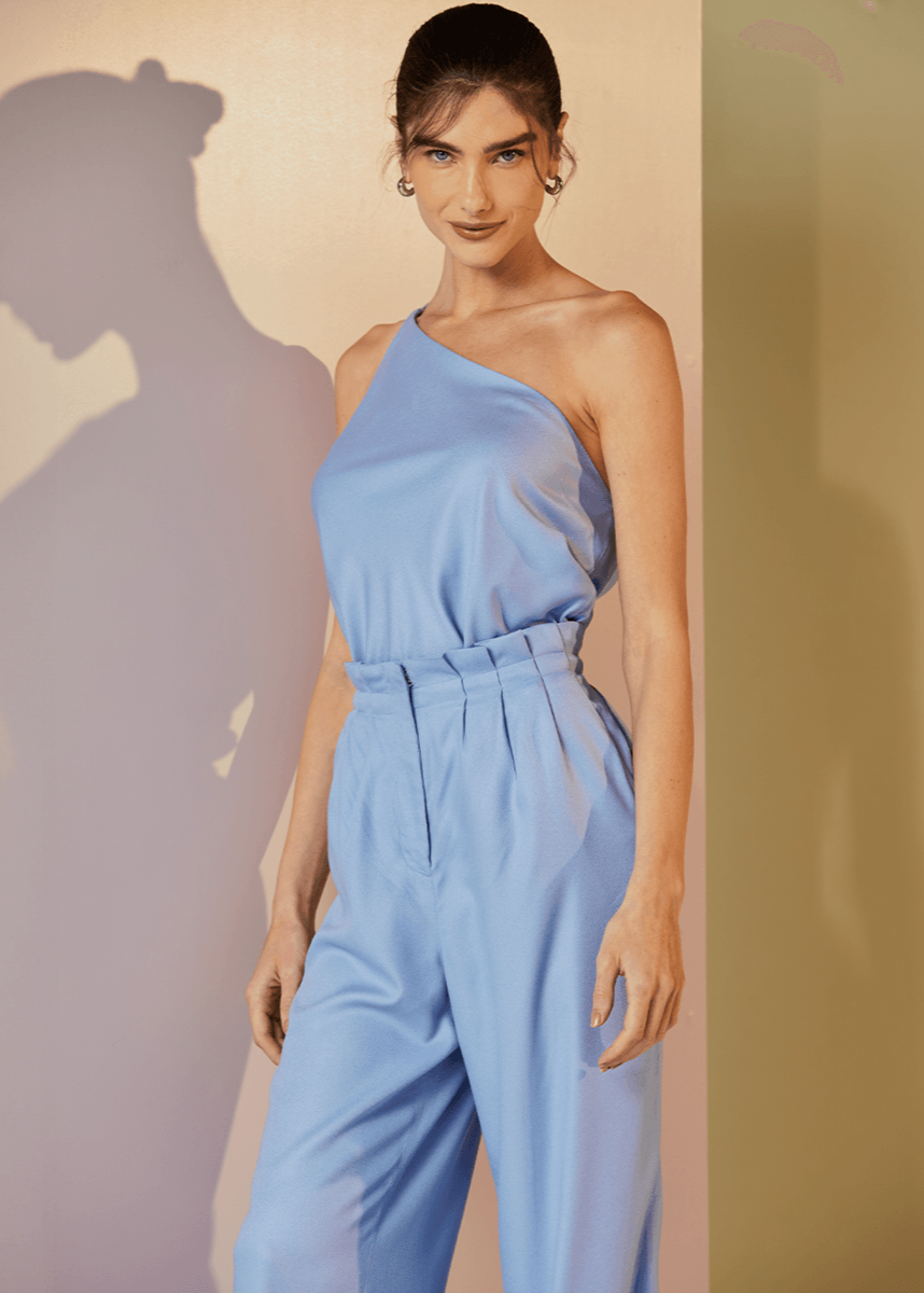 Woman wearing a light blue one-shoulder jumpsuit against a plain background