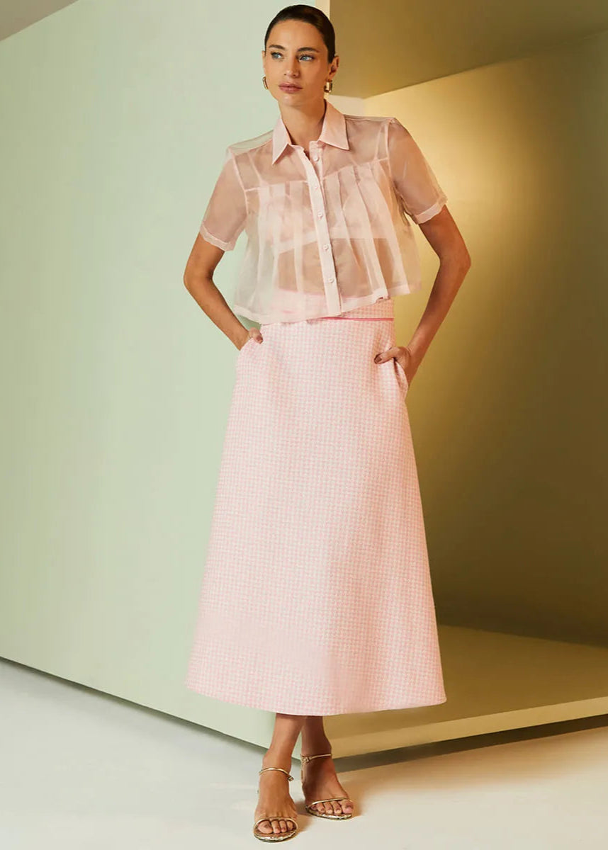 Woman wearing a light pink outfit with sheer top and striped skirt against a minimal background