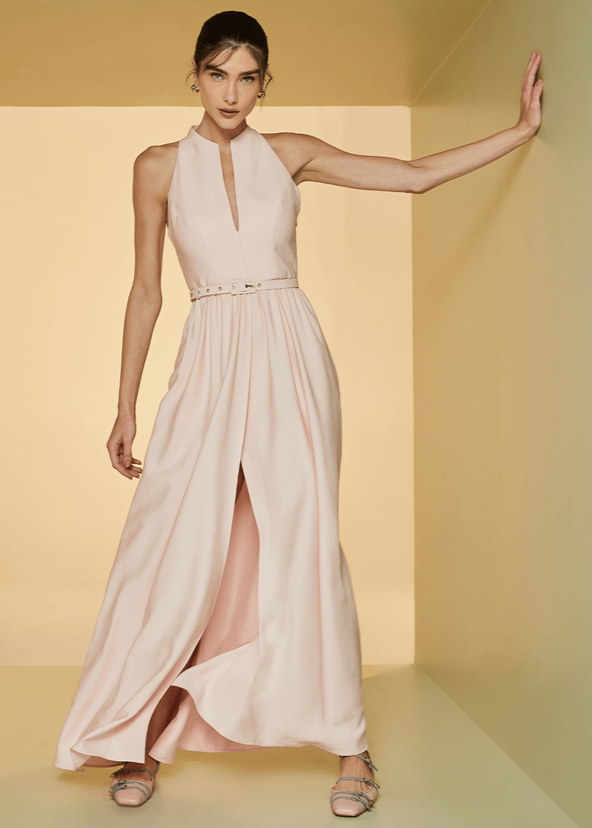 Woman wearing a light pink sleeveless dress with a slit in a yellow room.