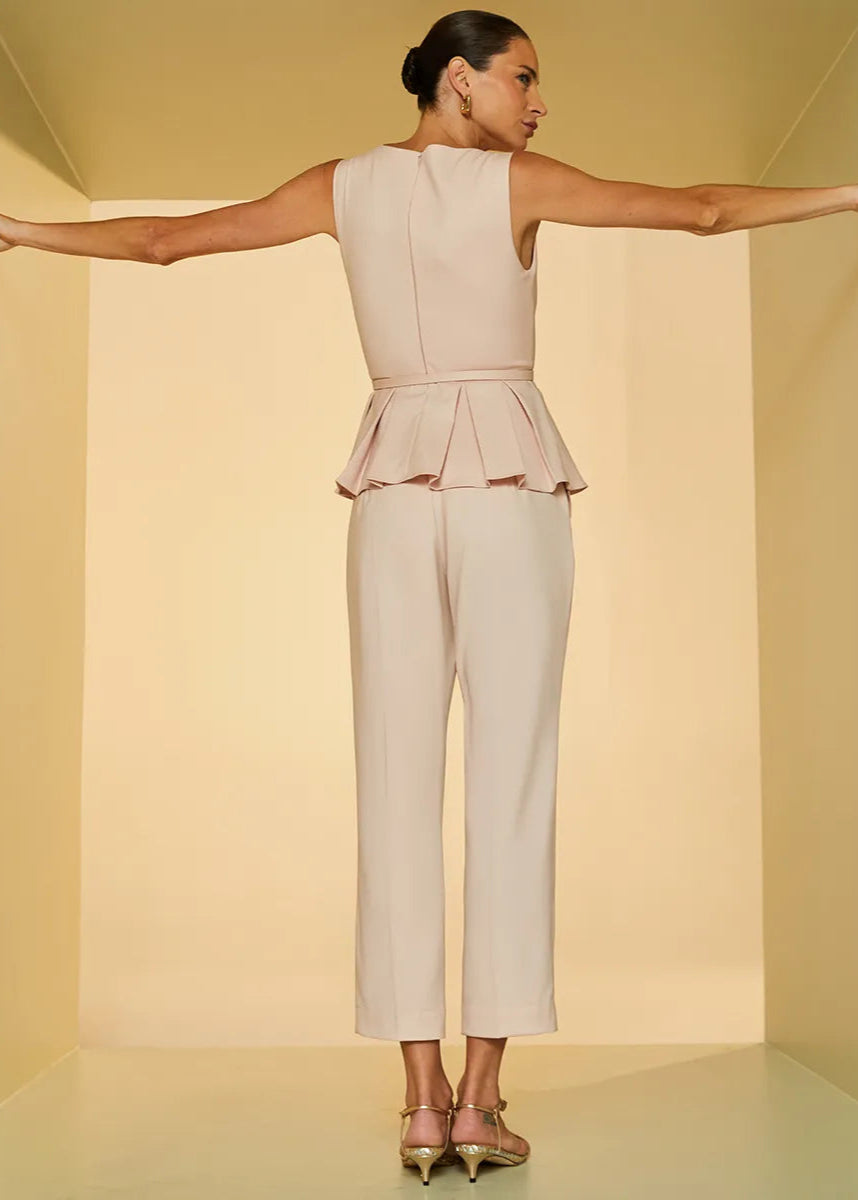 Woman wearing a beige peplum top and pants against a plain background