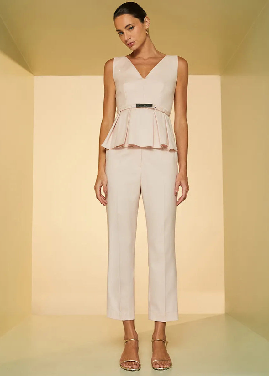 Woman wearing a beige peplum top and pants in a minimalistic setting