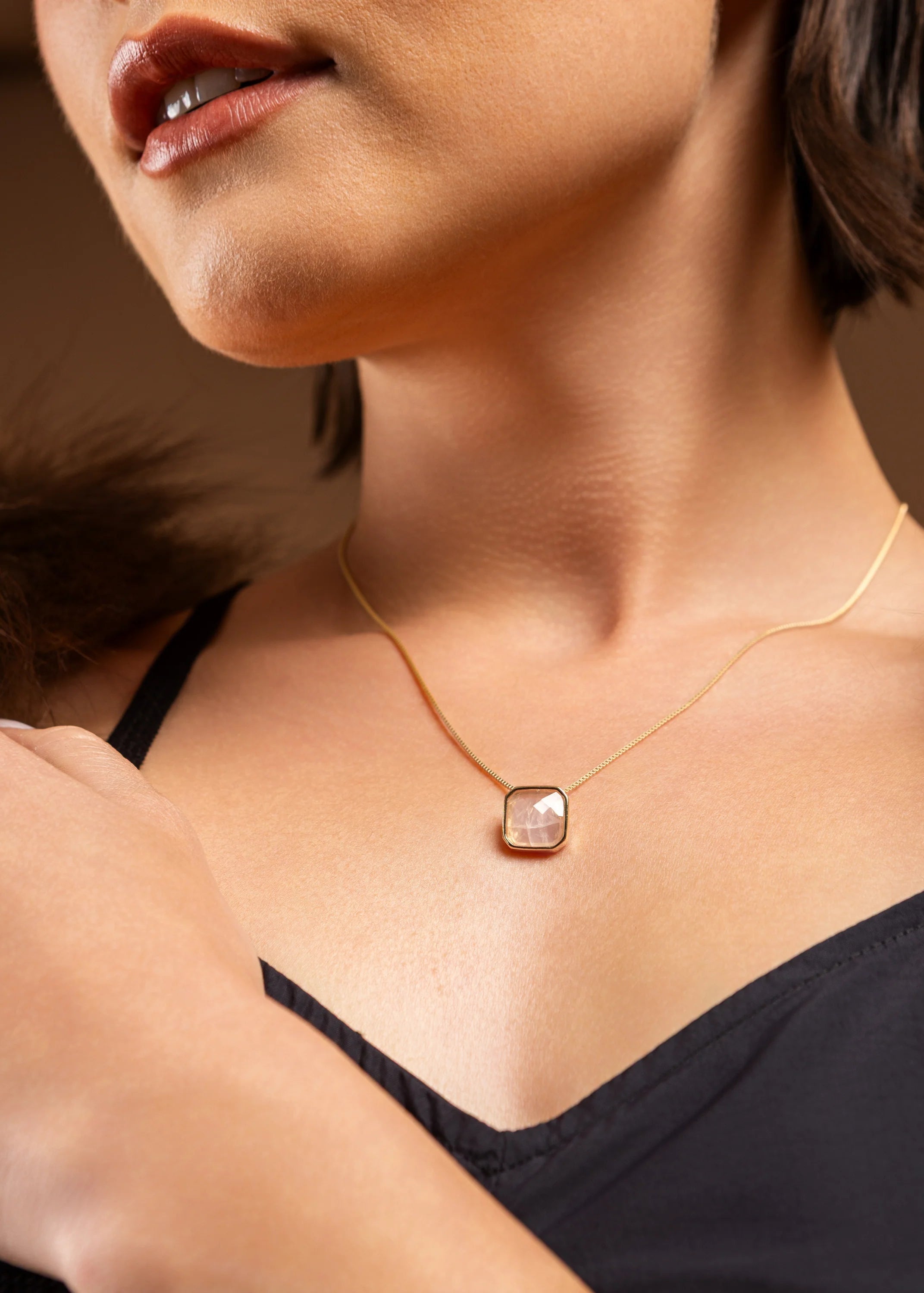 Close-up of a person wearing a gold necklace with a square pendant.