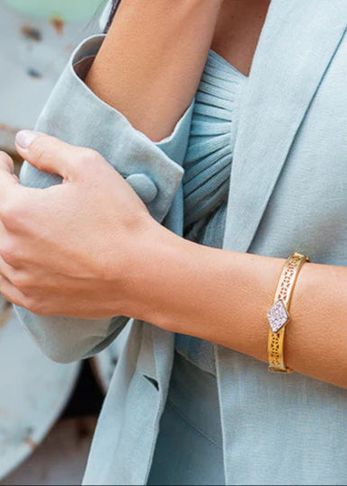 Person wearing a light blue blazer and gold bracelet with a blurred background