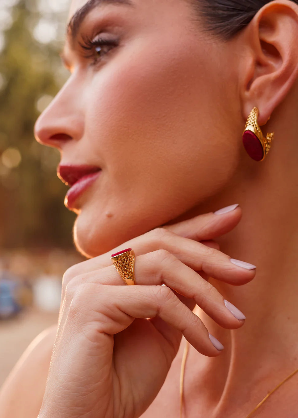 Close-up of a woman wearing gold earrings and ring with a blurred outdoor background