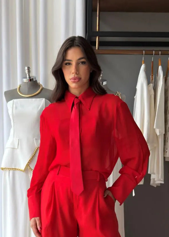 Woman in a red outfit standing in a room with white curtains and clothing racks.