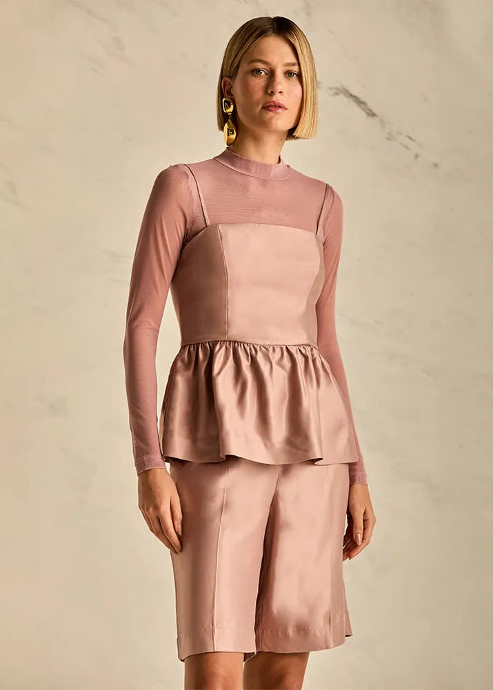 Woman wearing a pink peplum top and shorts against a neutral background