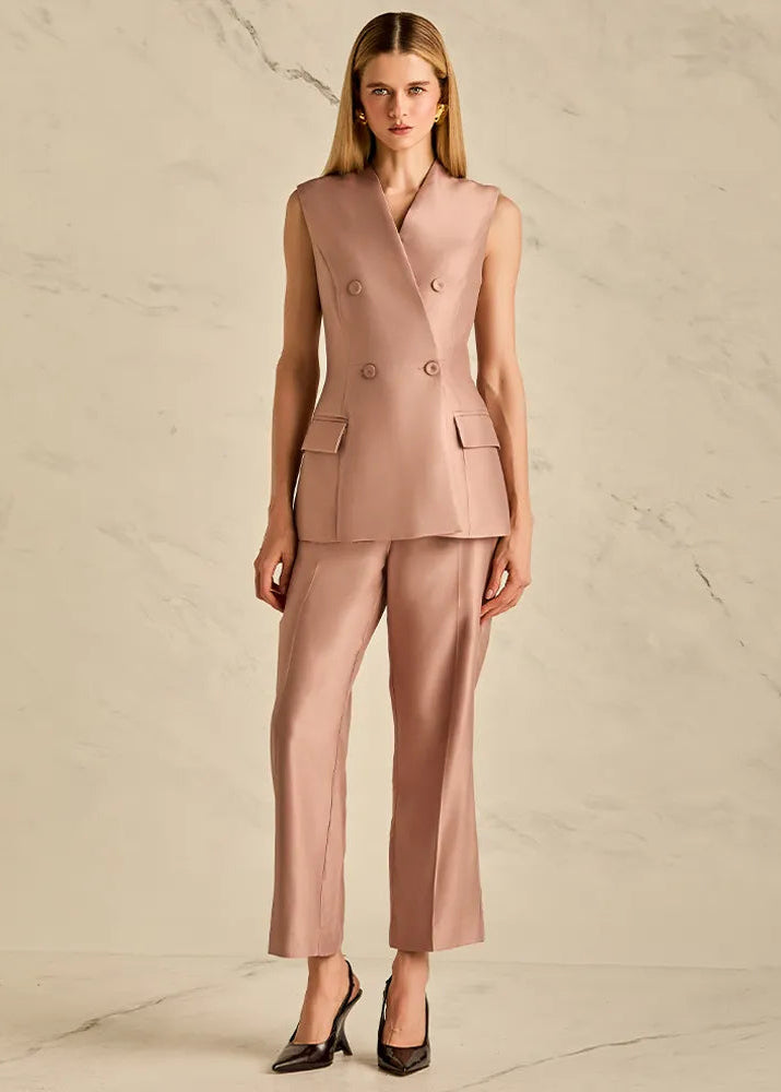 Woman wearing a pink suit with a vest and pants on a beige background