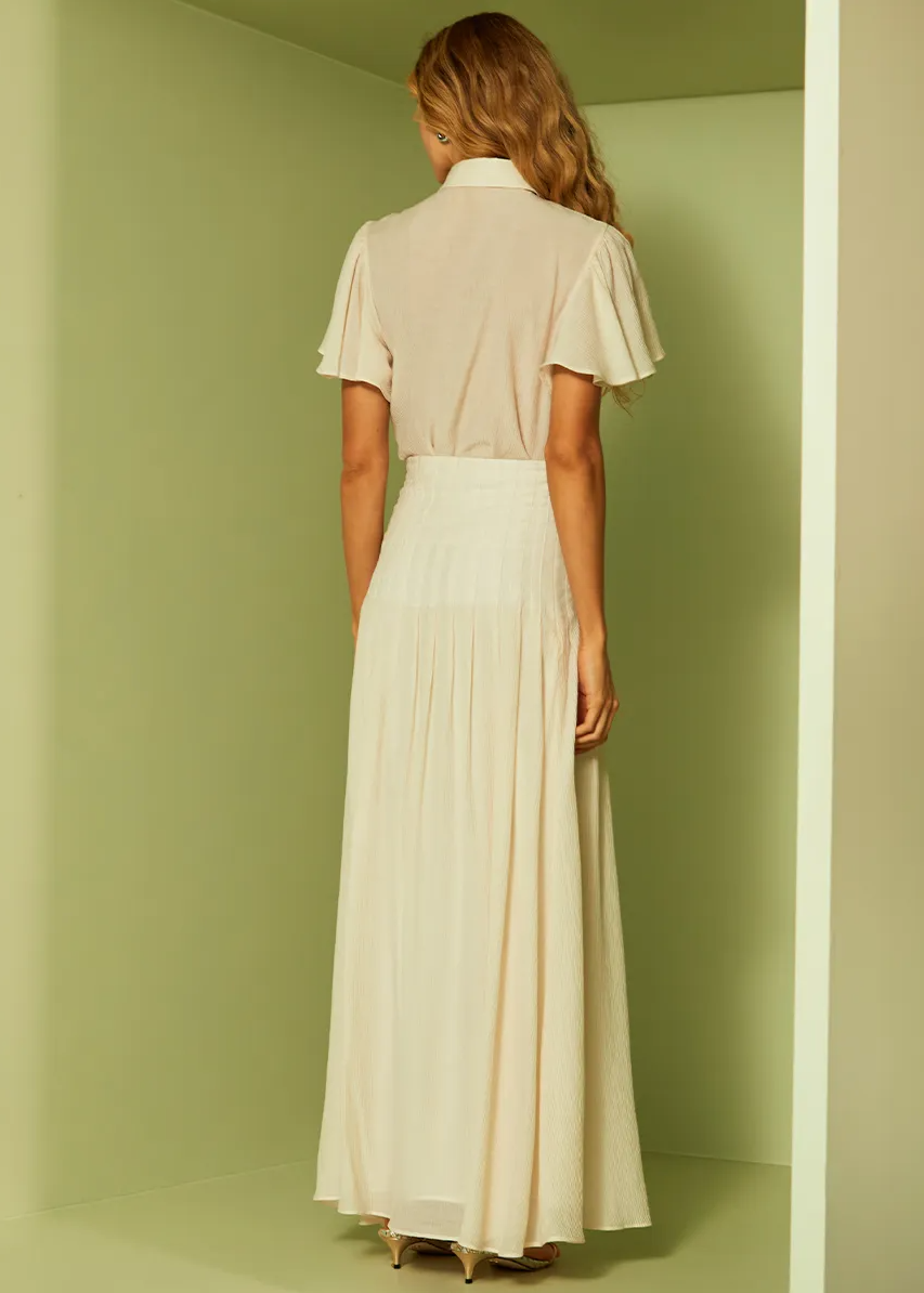 Woman wearing a beige blouse and white skirt standing in a room with green walls.