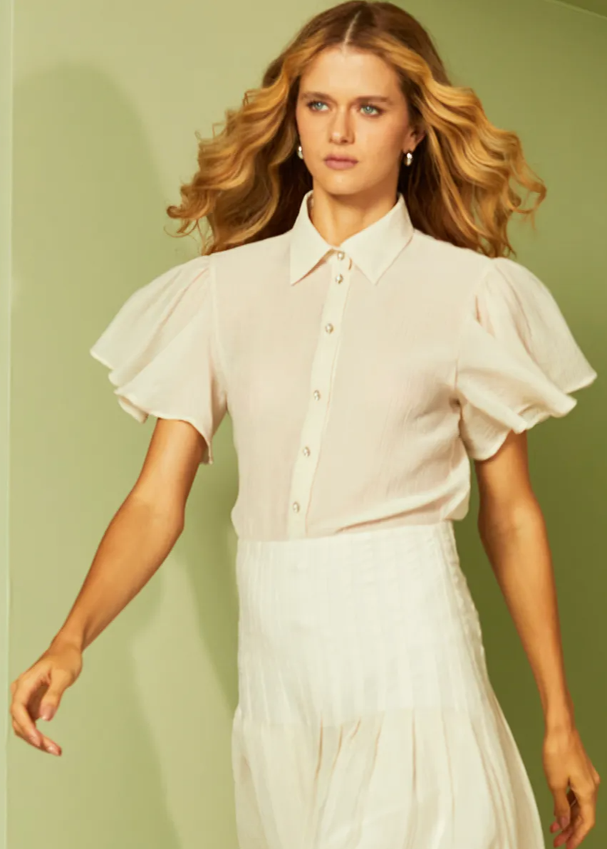 Woman wearing a white blouse with ruffled sleeves against a green background