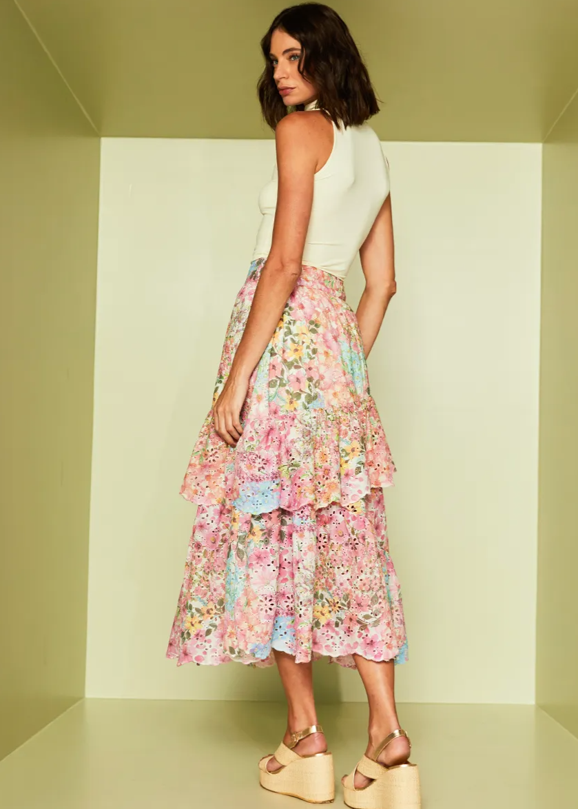 Woman wearing a light green sleeveless top and a colorful floral skirt against a plain background