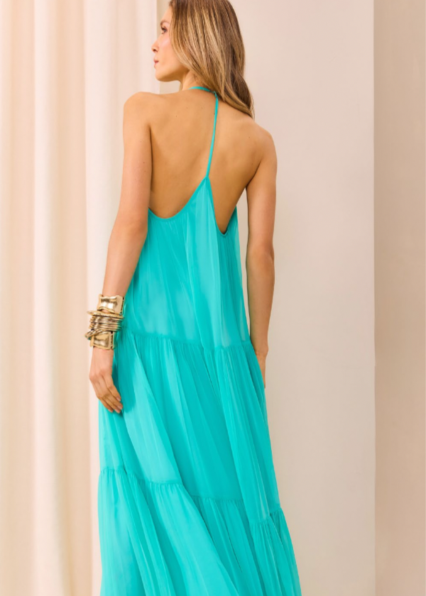 Woman wearing a turquoise dress with thin straps against a beige curtain background