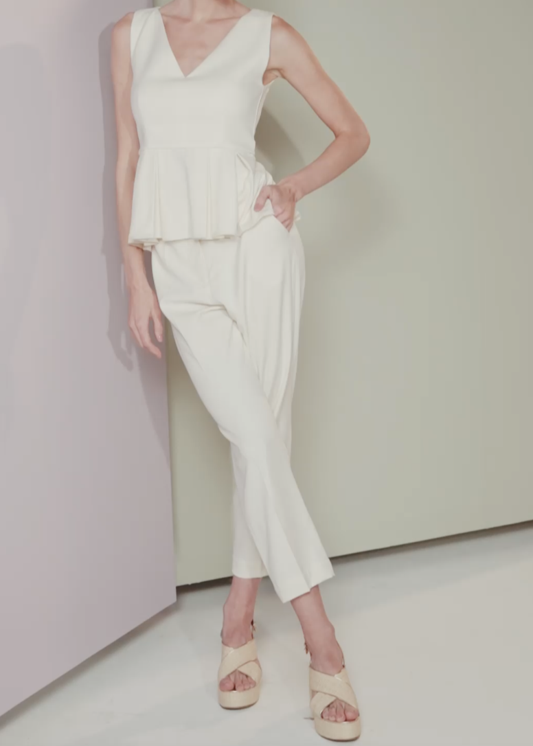 Woman wearing a white sleeveless top and pants against a plain background