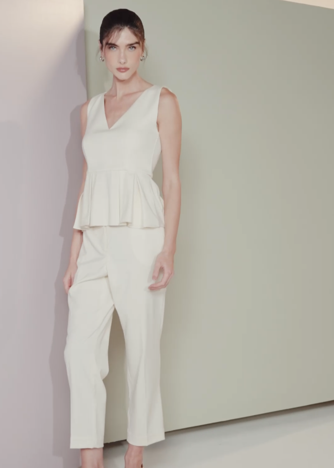 Woman wearing a white sleeveless top and pants against a plain background