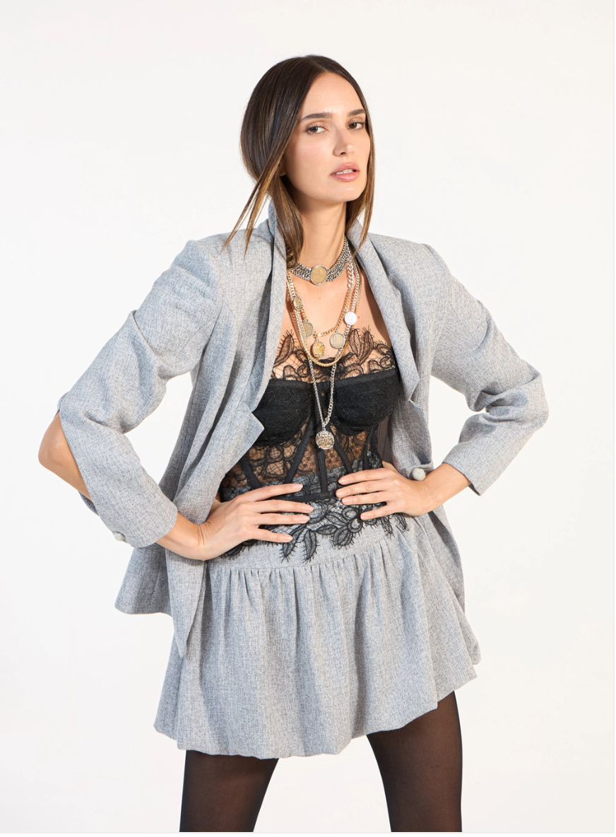 Woman wearing a gray blazer over a black lace top on a white background
