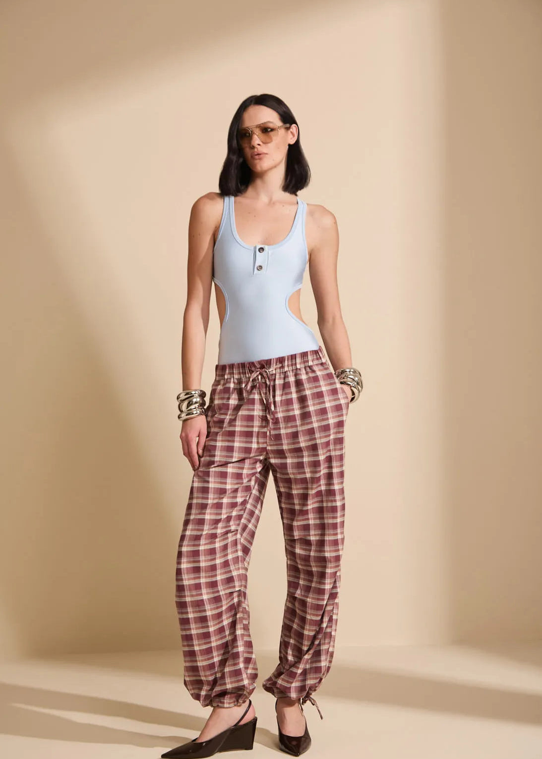 Woman wearing a light blue tank top and plaid pants against a beige background