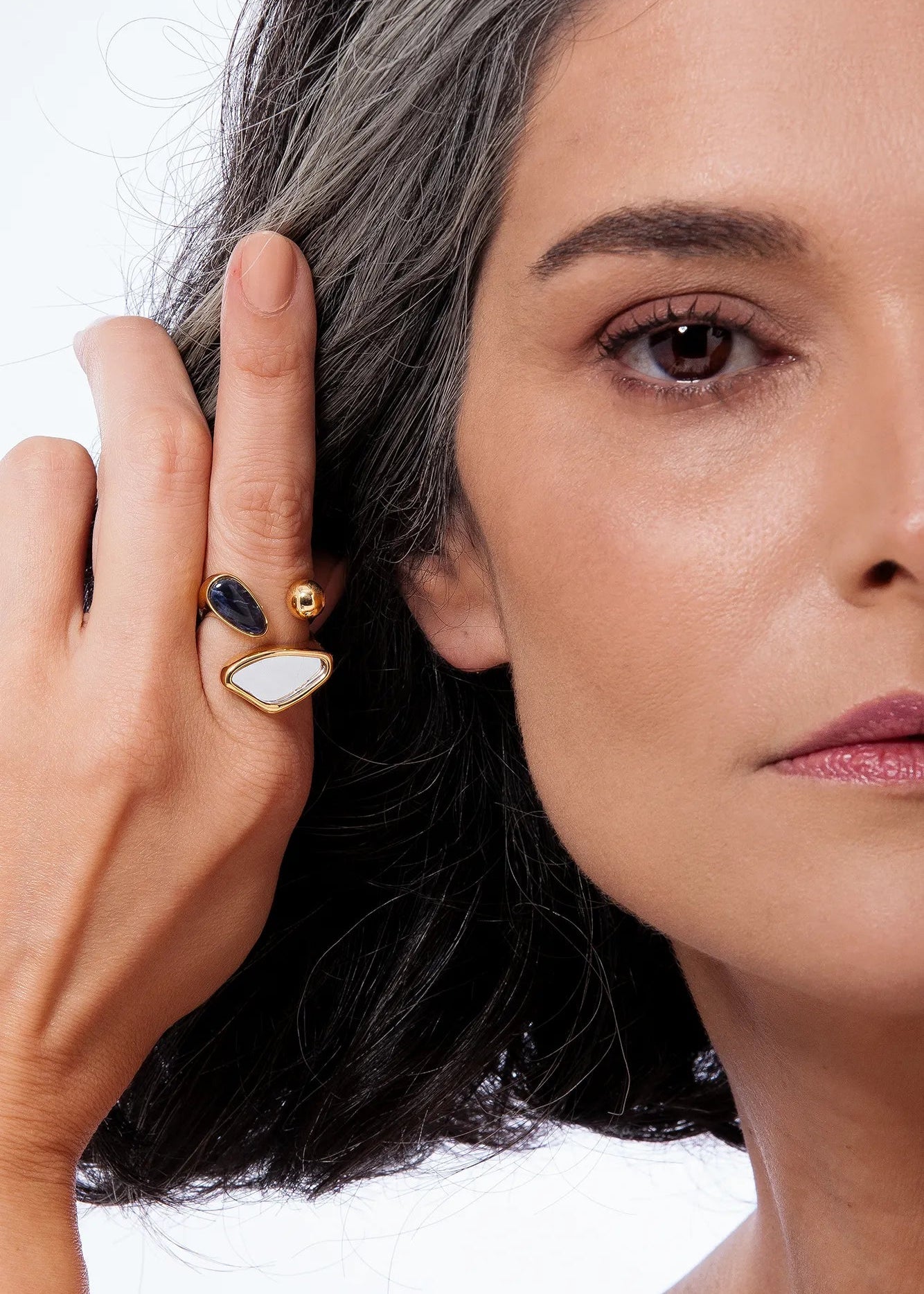 Woman wearing a gold earring with a white stone and black accent.