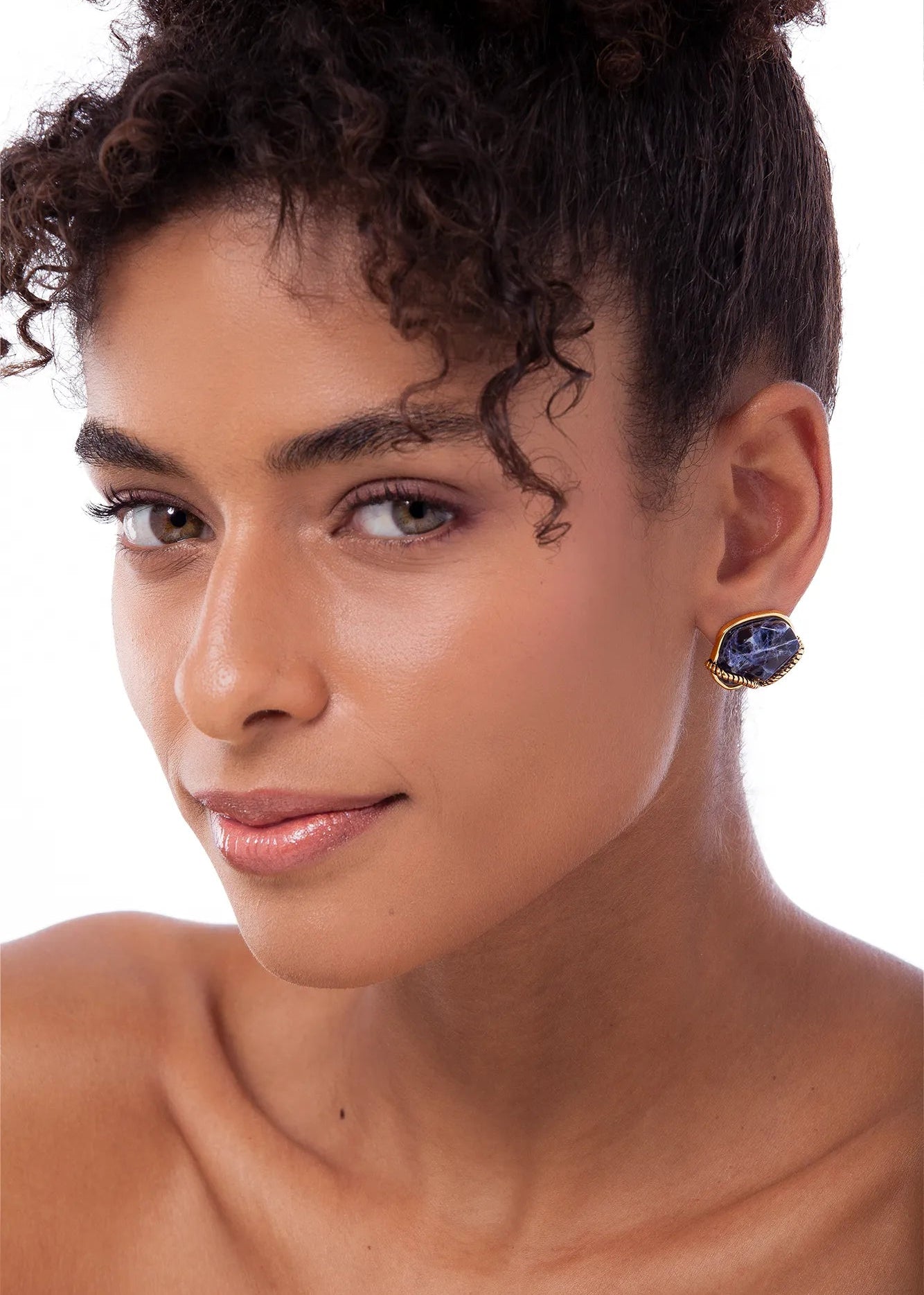 Close-up of a person wearing an earring with a blue gemstone on a white background
