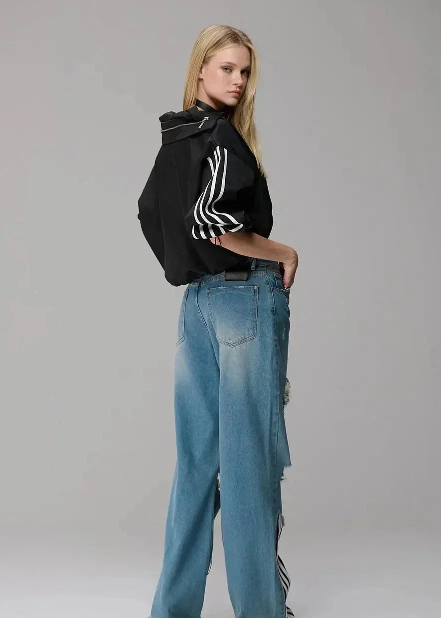 Person wearing a black jacket with white stripes and blue jeans on a gray background