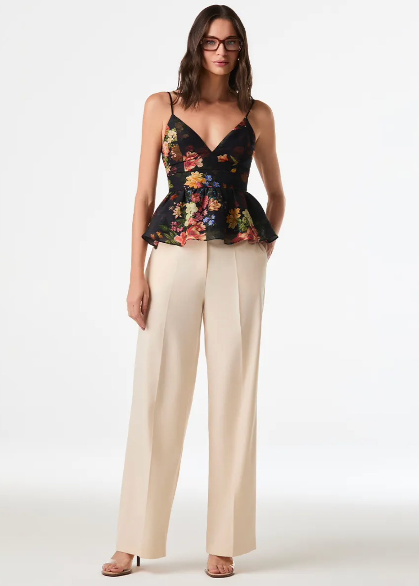 A model wearing a black floral corset-style camisole top with a peplum hem and cream wide-leg trousers, standing against a plain white studio background.