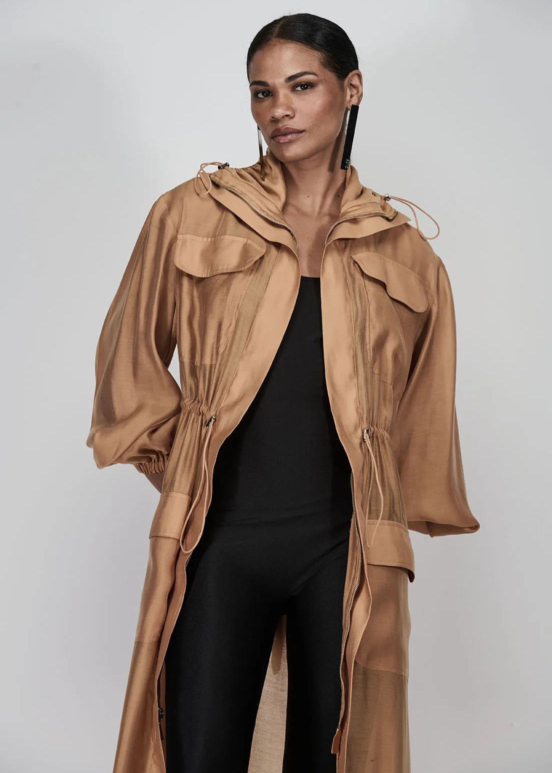Woman wearing a long beige coat over a black outfit on a white background