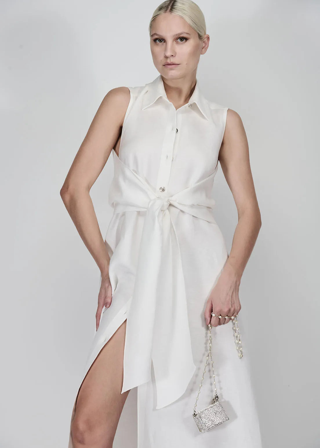 Woman wearing a white sleeveless dress with a high slit on a plain background