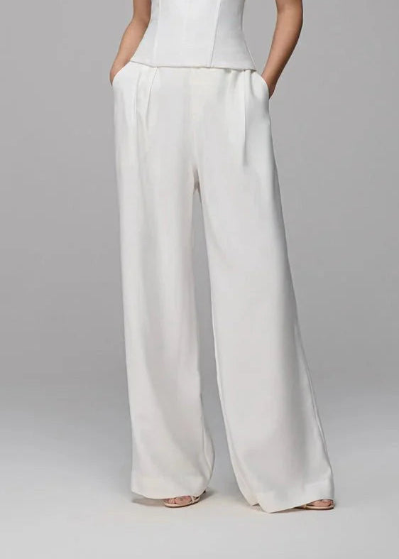 Woman wearing a white halter top and wide-leg pants on a gray background