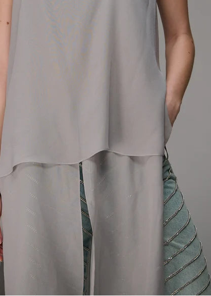 Woman wearing a strapless gray top and high-waisted pants against a gray background
