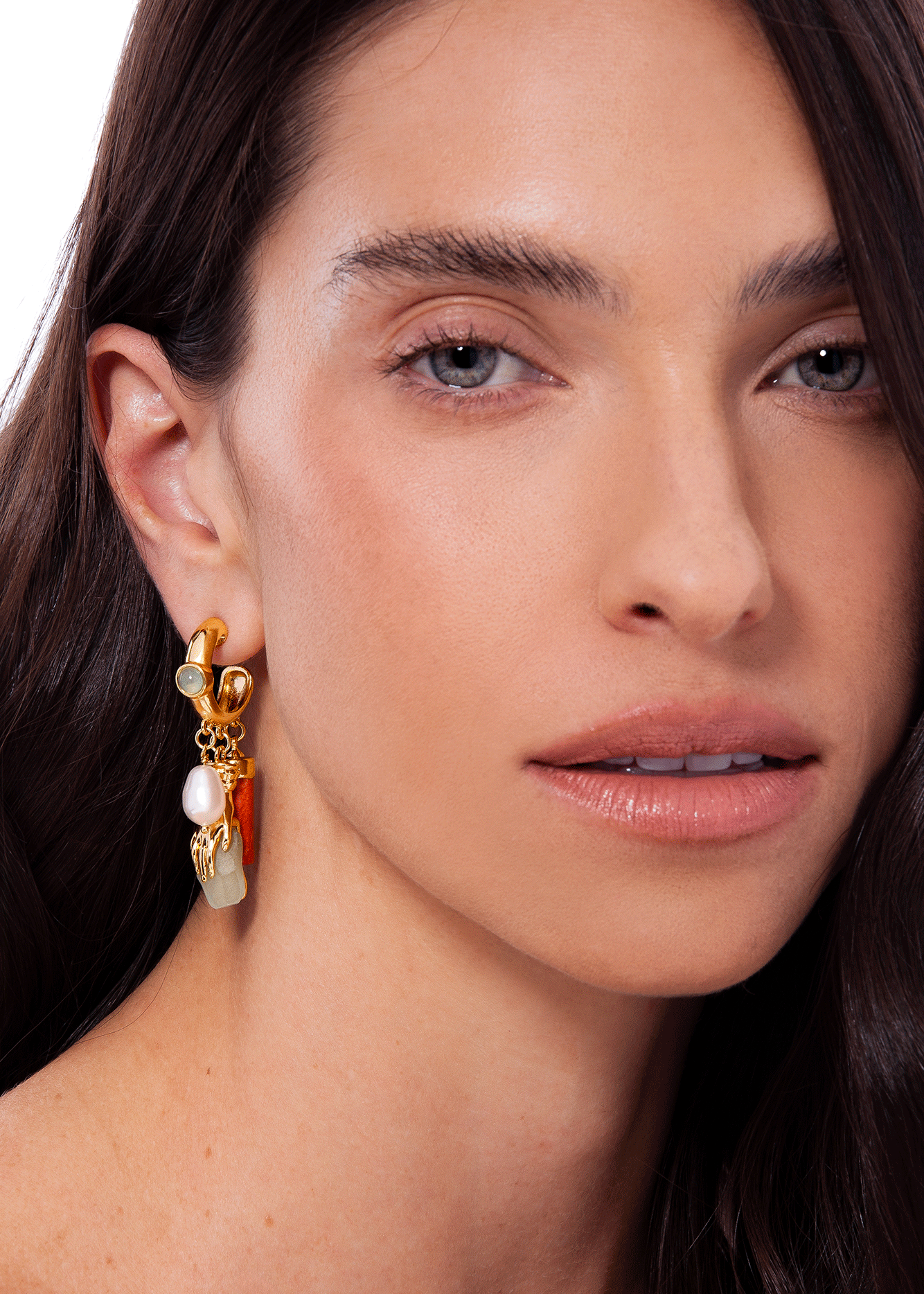Close-up of a woman wearing gold earrings with pearls and an orange gemstone.