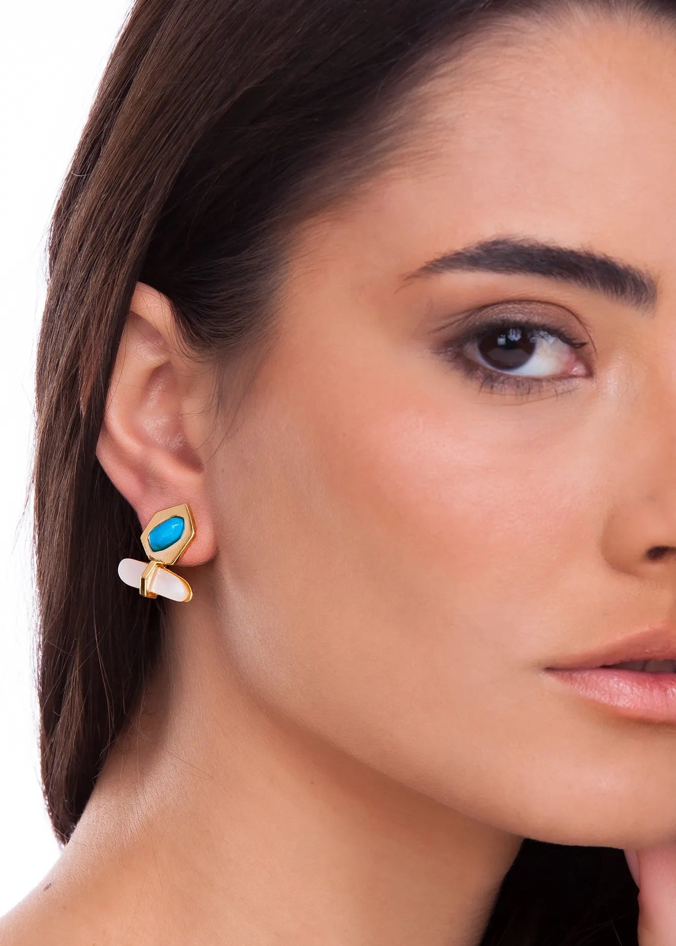 Close-up of a woman wearing a gold earring with a blue gemstone on a white background