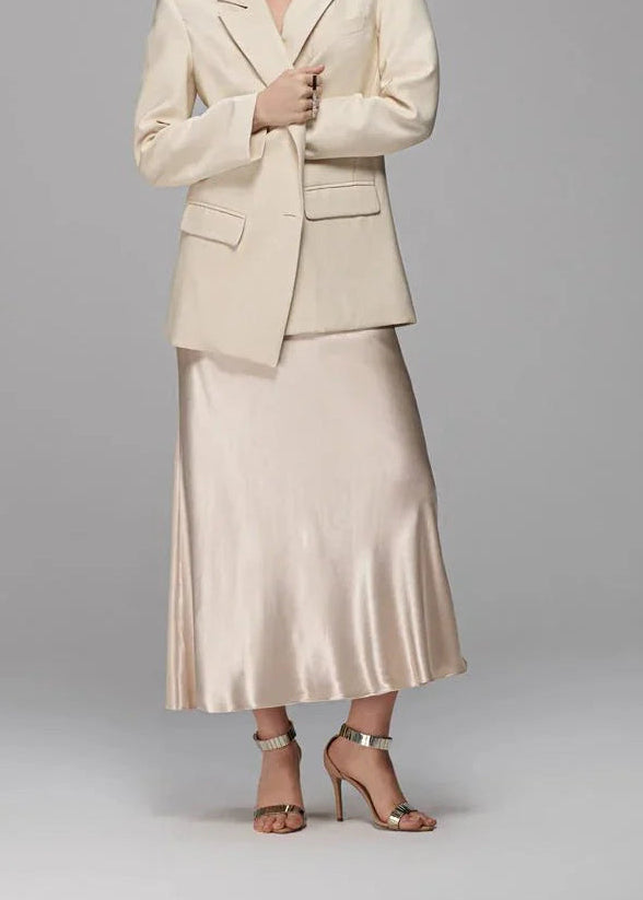 Woman wearing a beige suit with a satin skirt on a gray background