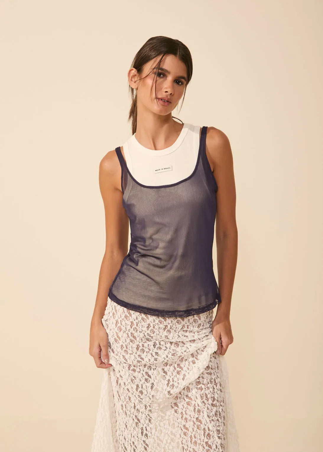 Woman wearing a sleeveless top and lace skirt on a beige background