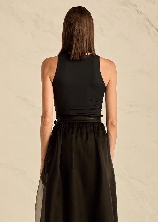 Woman wearing a black sleeveless top and long black skirt on a beige background