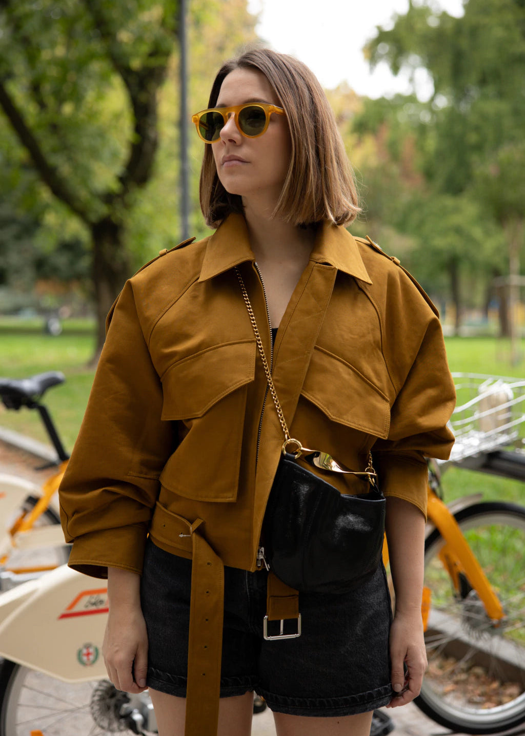 woman using a black leather bag with golden strap hardware with trees on the background