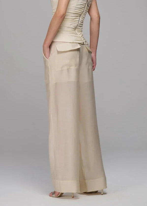 Woman wearing a beige strapless top and wide-leg pants on a gray background