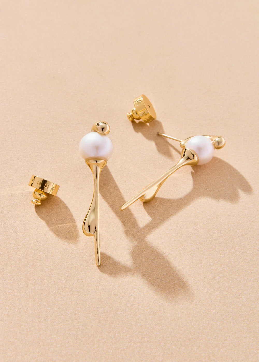 Gold earrings with pearl-like beads on a beige background