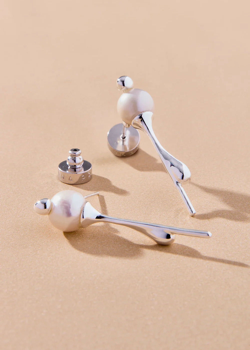 Pair of silver earrings with pearl-like beads on a beige background