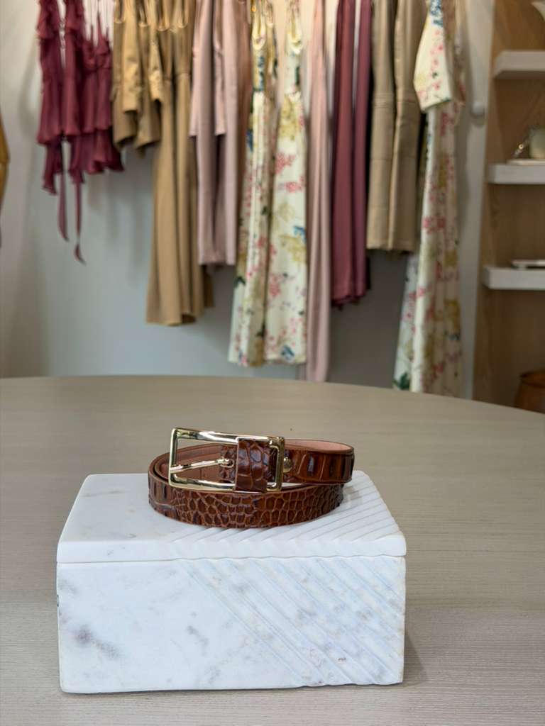 Brown leather belt on a white marble block with clothing in the background