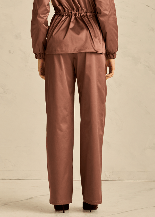 Woman wearing a brown raincoat and pants set against a beige background