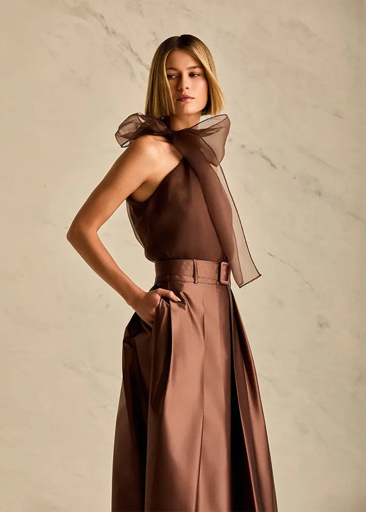 Woman wearing a brown blouse with a large bow against a beige marble background