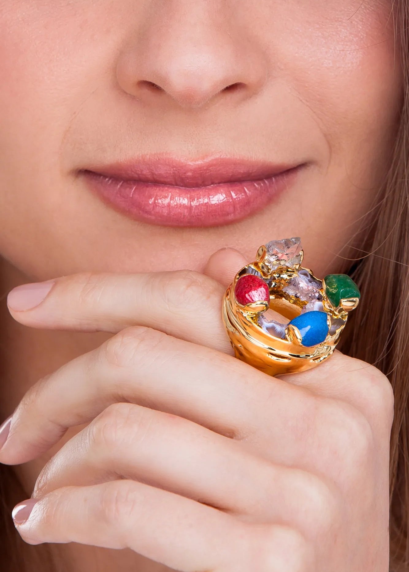 Close-up of a hand wearing a colorful gemstone ring with a blurred background