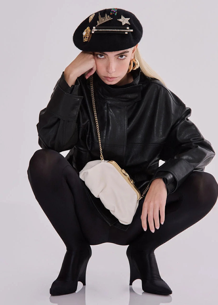 Person wearing a black outfit with a white handbag, sitting on a white background