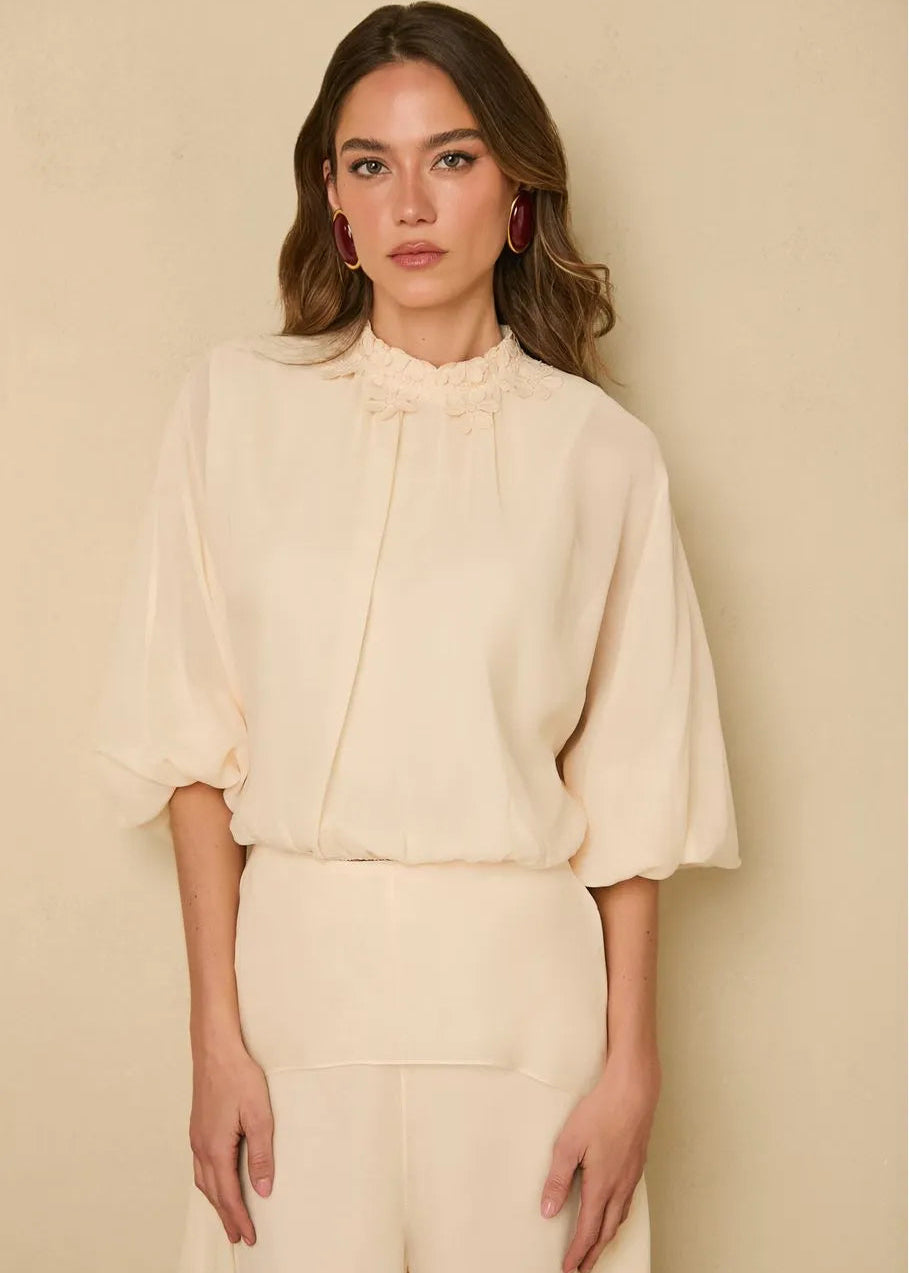 Woman wearing a cream blouse and pants against a beige background