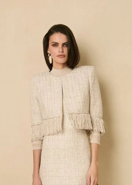 Woman in cream color tweed jacket sanding next to old suitcases against a beige background