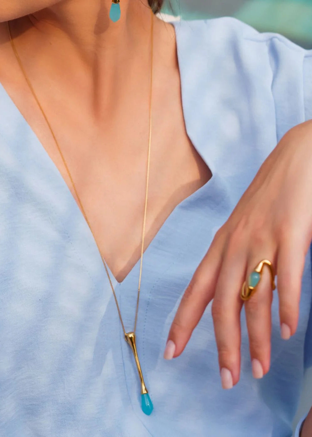 Close-up of a necklace with a blue pendant and a gold ring on a light blue background