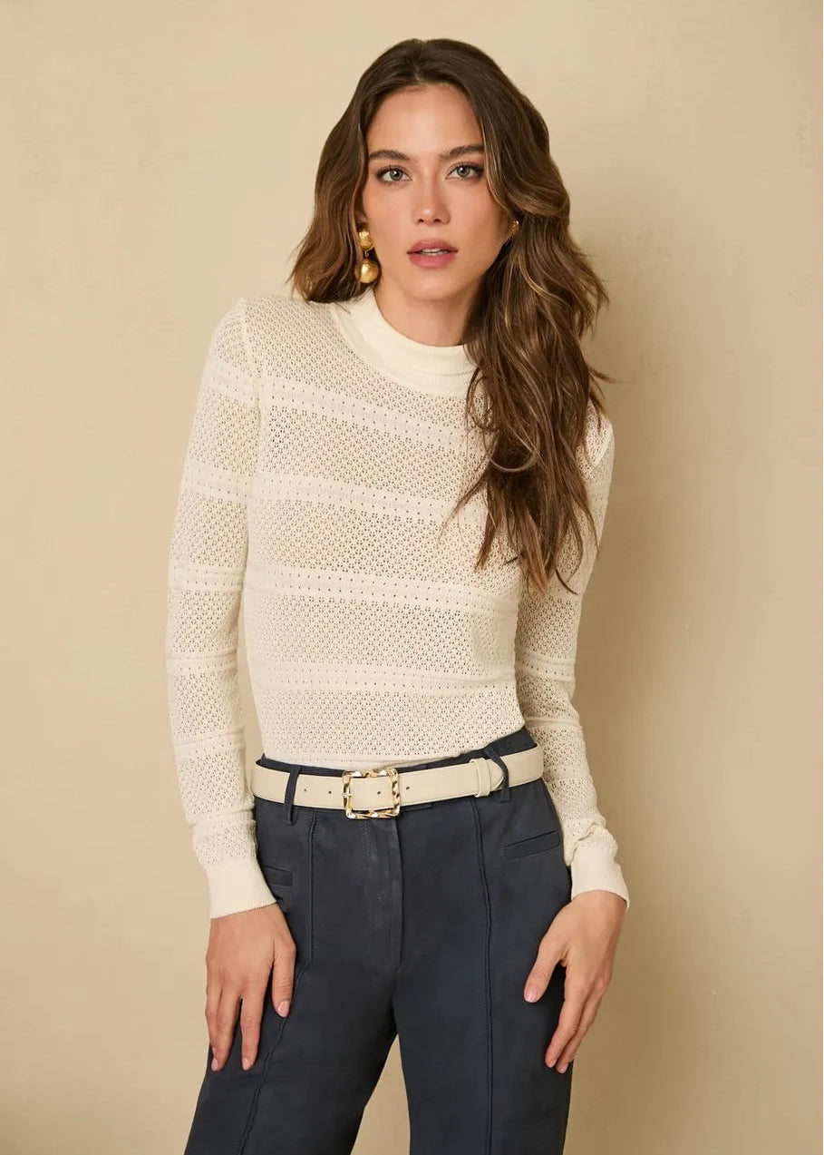 Woman wearing a cream sweater and dark pants against a beige background