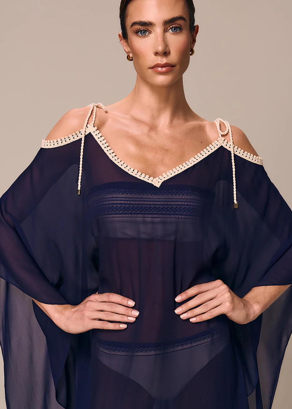 Woman wearing a dark blue off-shoulder top with lace details on a neutral background