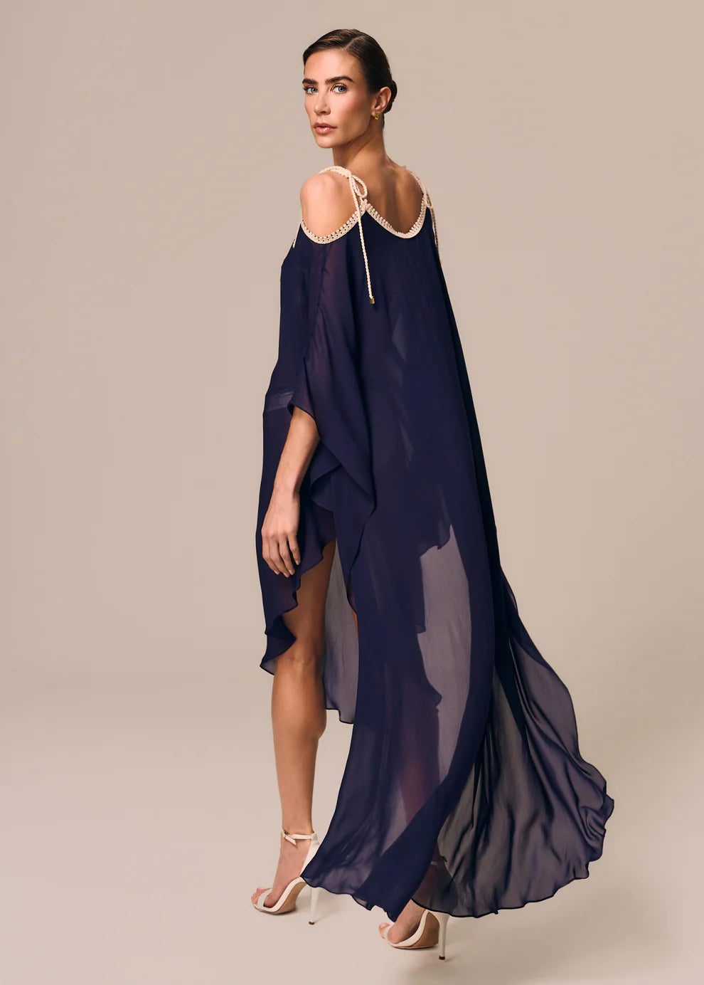 Woman wearing a navy blue dress with sheer overlay on a beige background