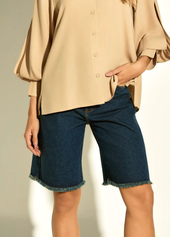 Woman wearing a beige blouse and denim shorts on a white background