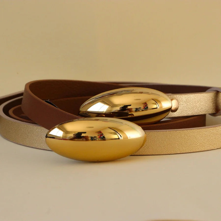 Gold belt buckles on a brown leather belt against a beige background